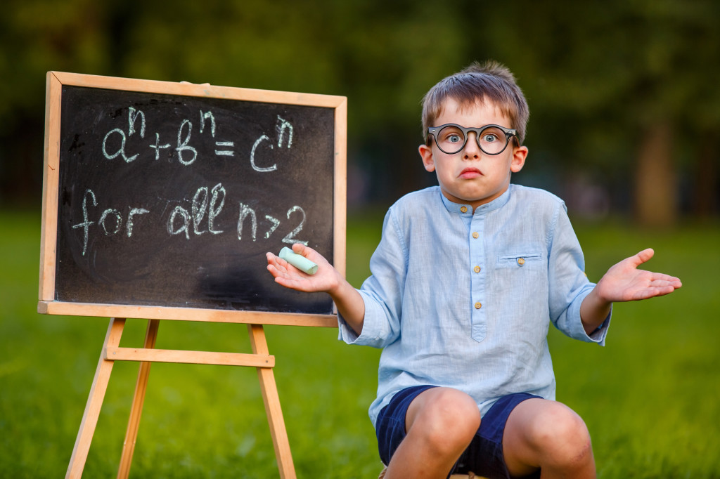 Cute little confused student shrugging his shoulders has no answer, thinking, puzzled